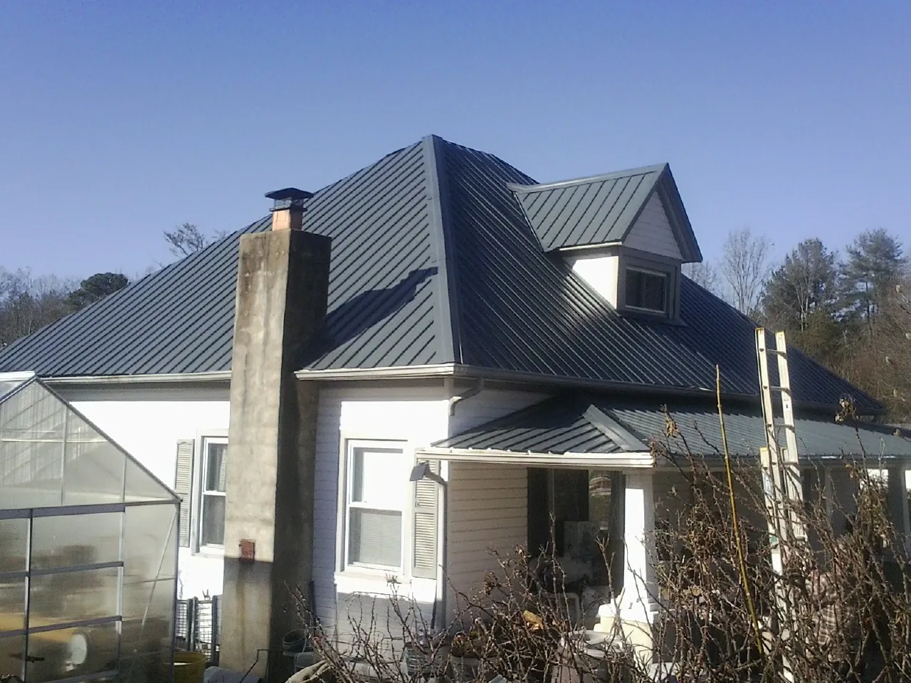 Dark blue standing seam metal roof on a white farmhouse with dormer — Slate & Tile Roof Repair by Roofing Brothers in Roby