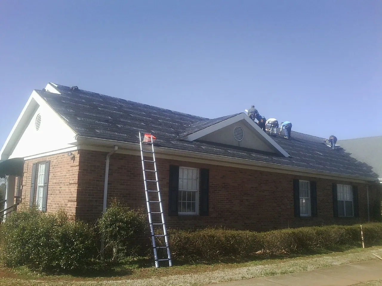 Crew tearing shingles off a brick ranch roof with a ladder set — Metal Roof Repair work by our crew in Roby