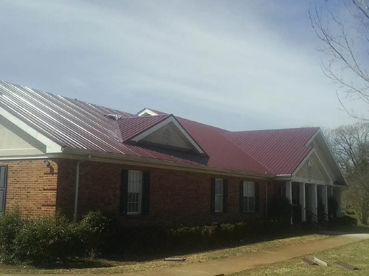 Red metal roof with gabled entries on a long brick building, from a Hail Damage Roof Repair job in Roby