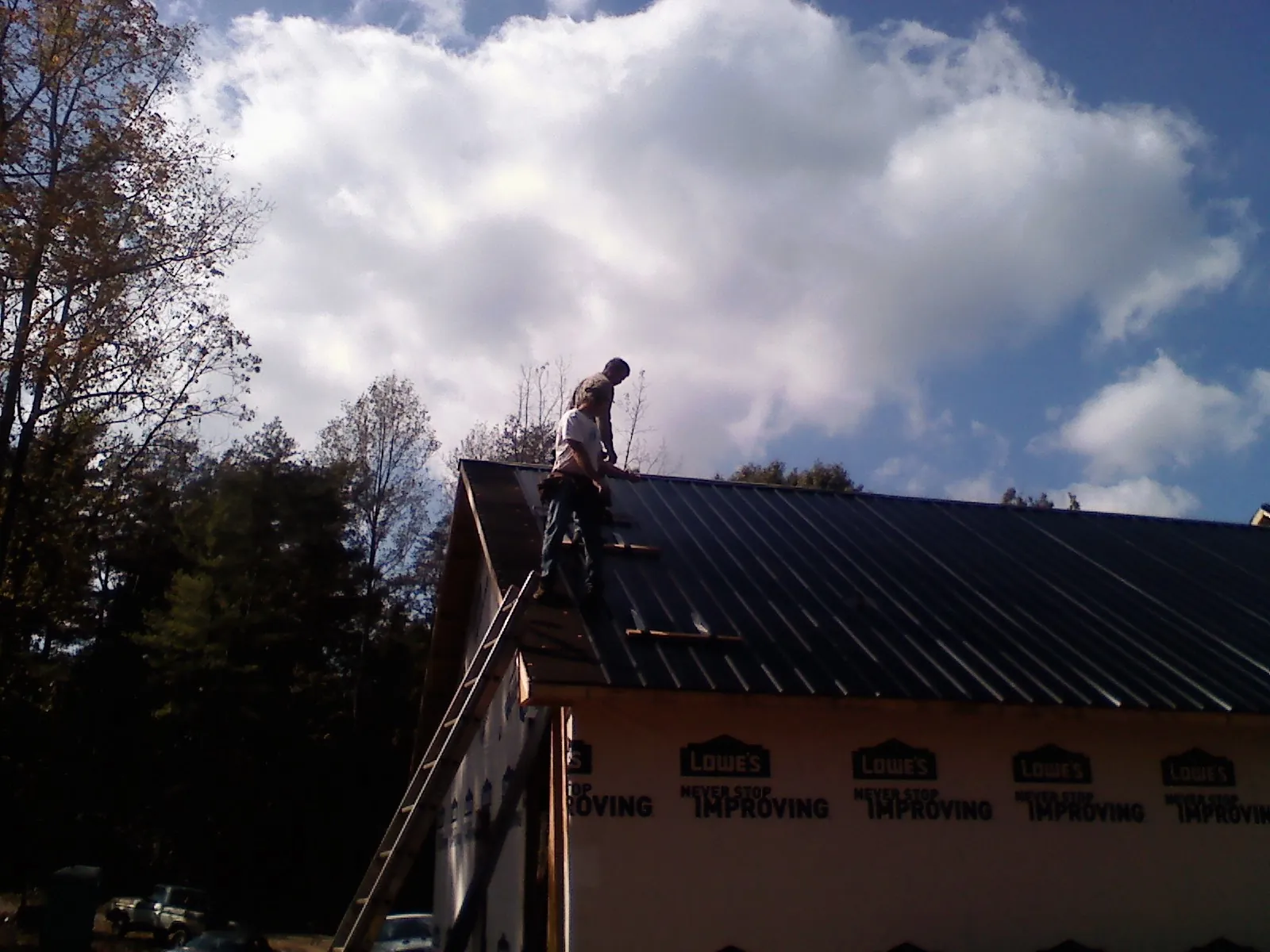 Roofer fastening dark metal panels high against a cloudy sky, from a Roof Inspection job in Roby