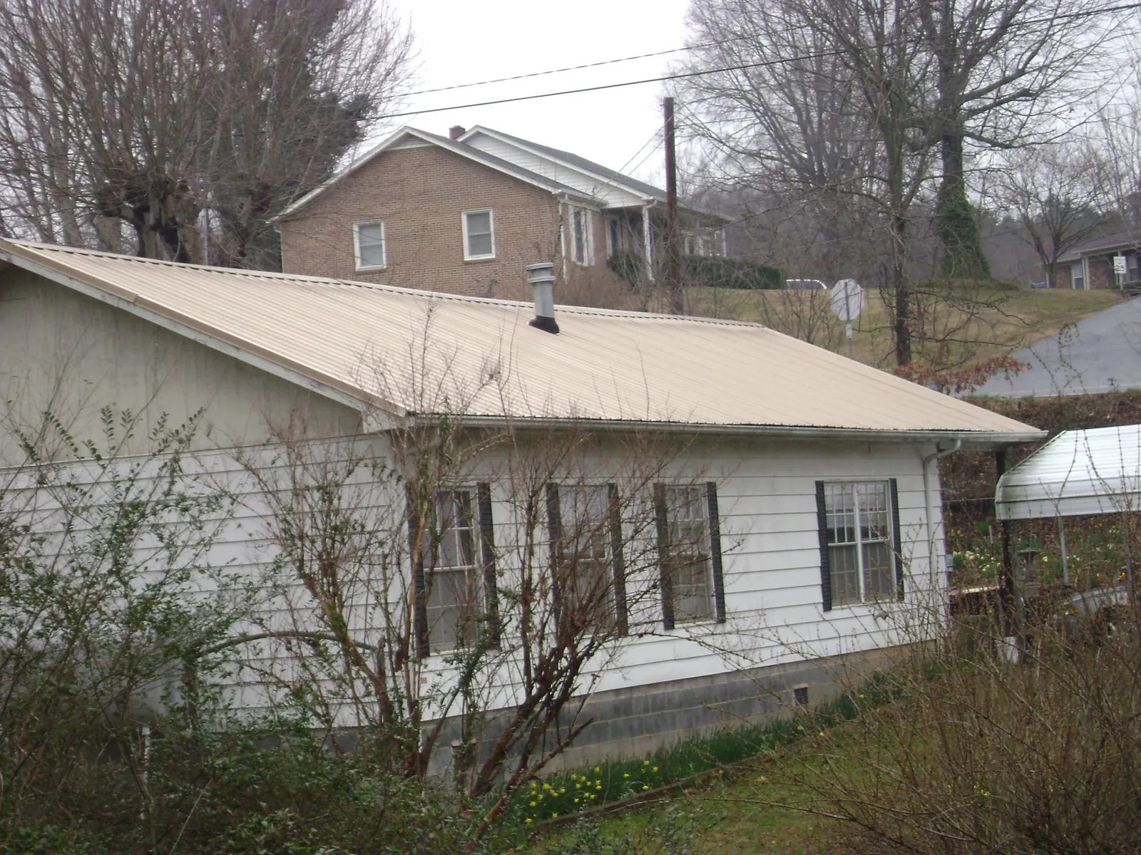 Tan metal roof on a white sided house set into a hillside — Commercial Roofing by Roofing Brothers in Roby